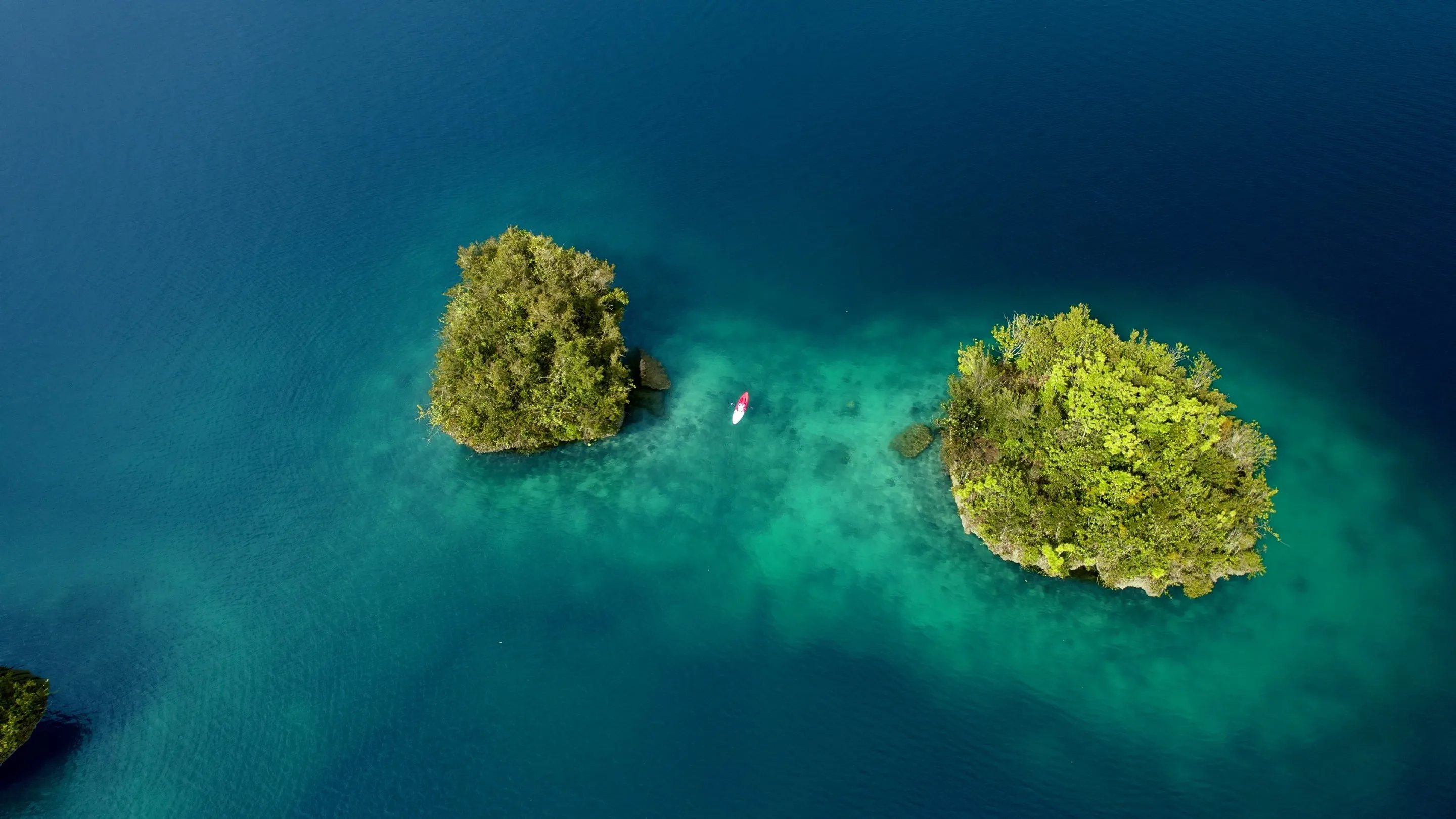 A kayak drifting between forested karst islands in glassy turquoise water