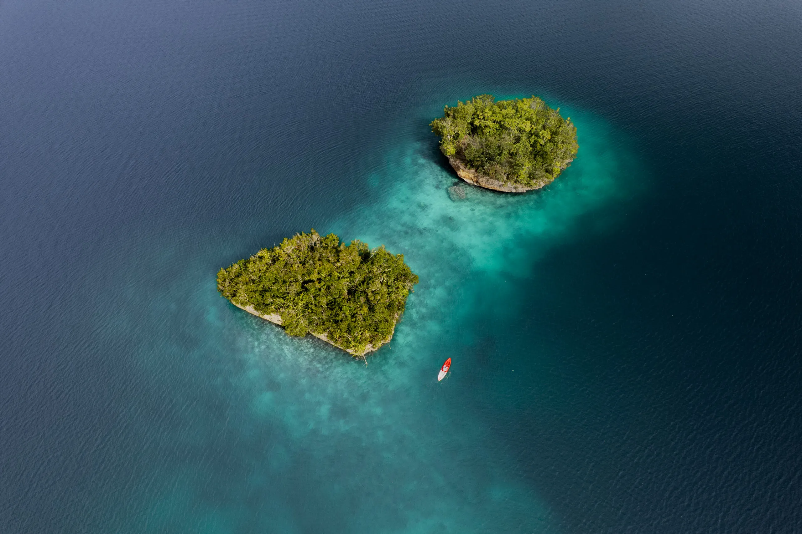 Aerial view of a kayak on deep calm water beside two small forested islets