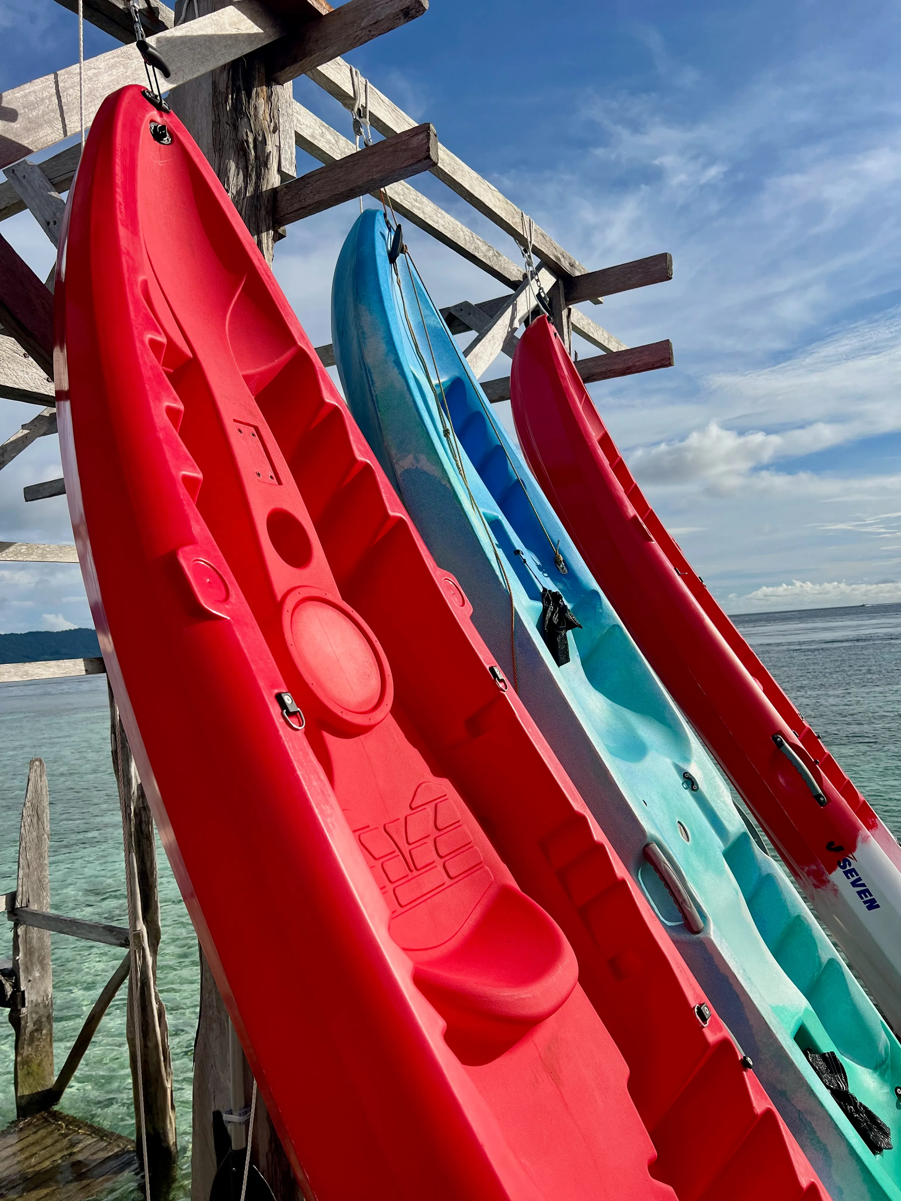 Red and blue kayaks hanging on the wooden jetty rack above clear shallow water